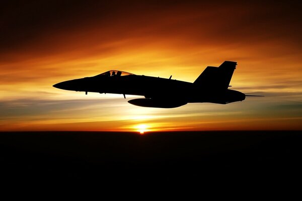 A military plane flies against the background of sunset