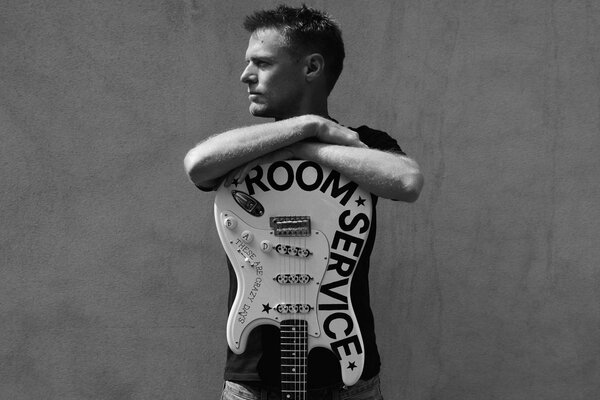 Bryan Adams con una guitarra en una pared gris