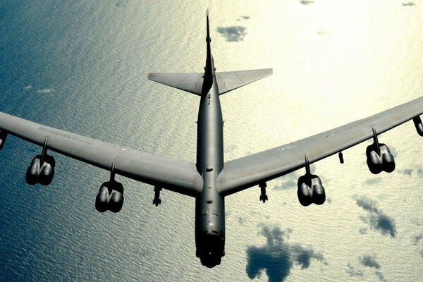 A huge military bomber is flying over the sea