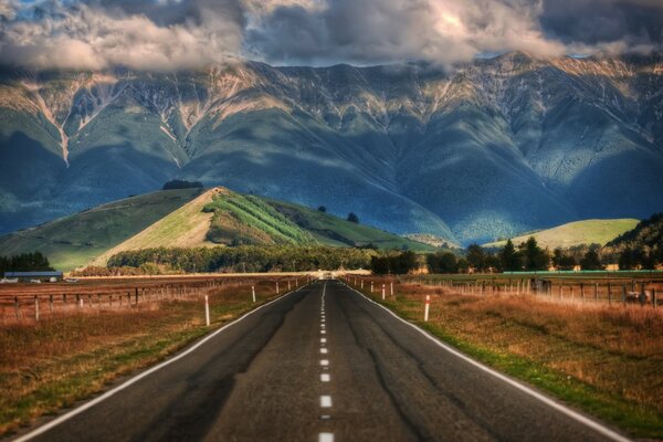 Carretera rodeada de campos con vistas a las colinas y montañas de Nueva Zelanda