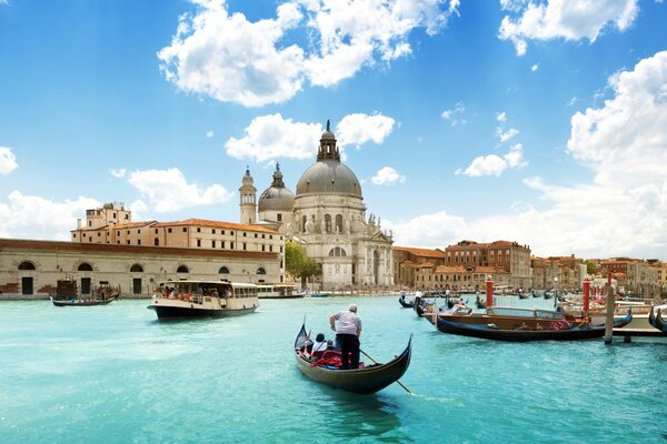 People are sailing on a gondola along the azure river towards the ancient cathedral