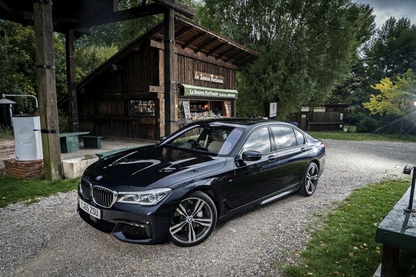 A black BMW car in an old parking lot with a shed