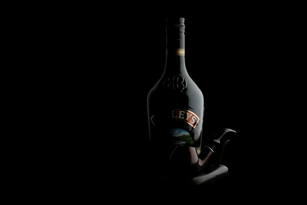 Botella de licor y tubo sobre un fondo oscuro