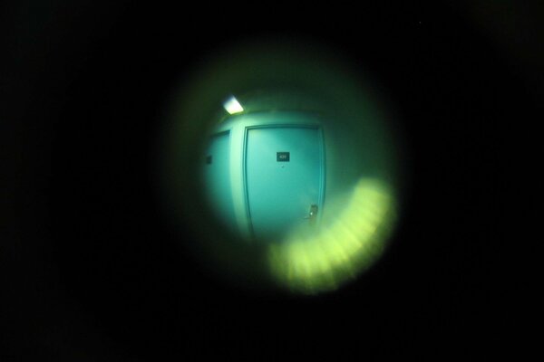 A lamp near the neighboring doors with a view through the peephole