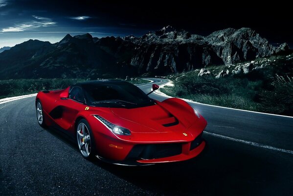 Ein roter Ferrari fährt auf einer nächtlichen Bergstraße