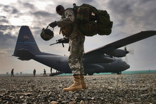 An armed soldier with a backpack near the plane