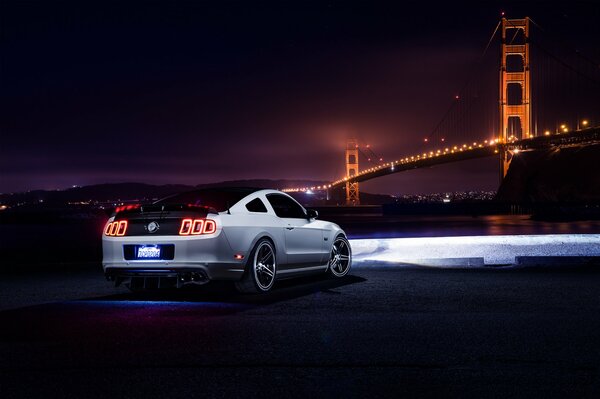 White Ford Mustang in the night, headlights illuminating the way to the bridge, rear view