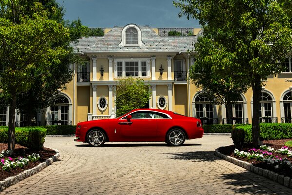 Ein Rolls-Royce2015 in leuchtend kramerfarbener Farbe steht in einem Park neben dem Haus