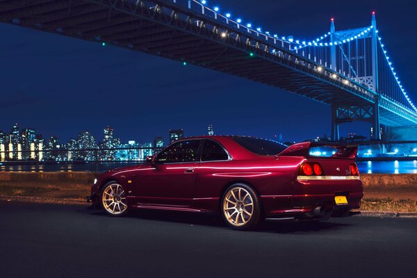 Une voiture nissan rouge se tient sous le pont de New York dans la nuit