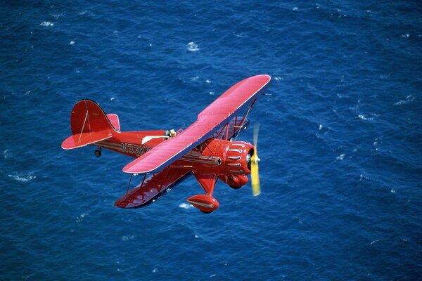 Un biplano rojo vuela sobre el mar