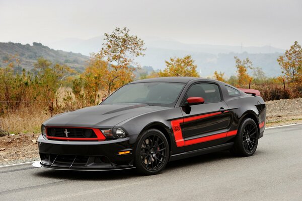 Black Ford Mustang with red tuning, front view, scenic highway