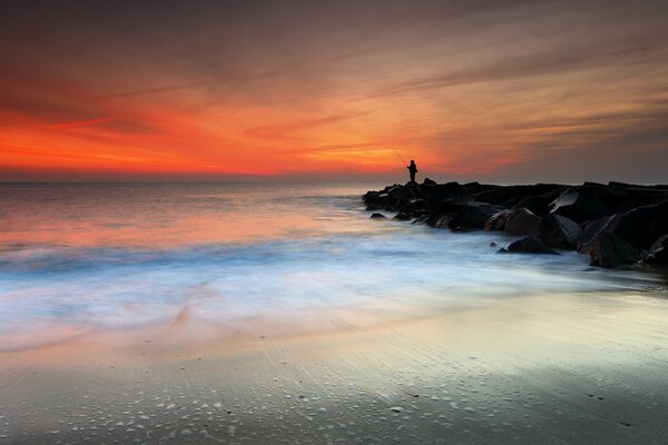 A fisherman standing on the rocks on the seashore