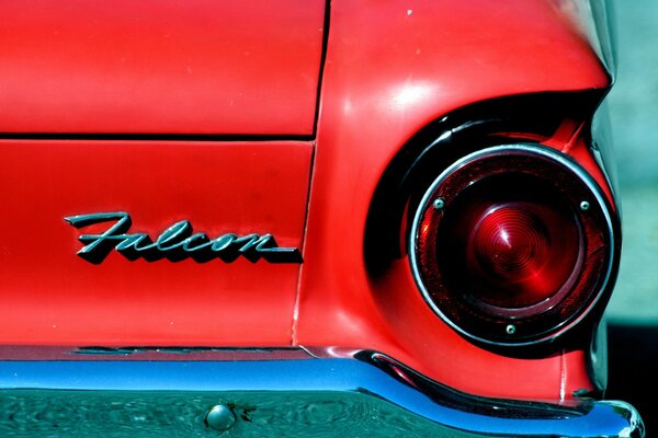 The rear of a red car with one headlight and a logo