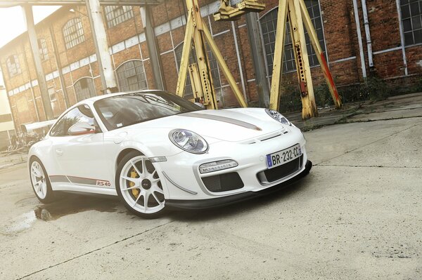 A white Porsche standing against the background of a brick factory