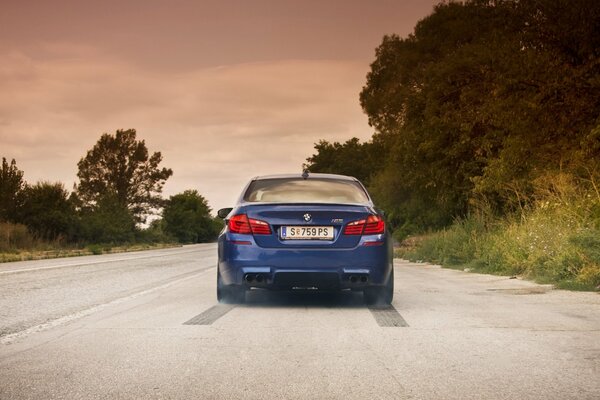 Niebieskie bmw na drodze z chmurami nieba