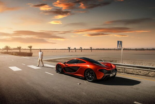 A red supercar on the road in the middle of the desert in front of a pedestrian crossing where a person is walking