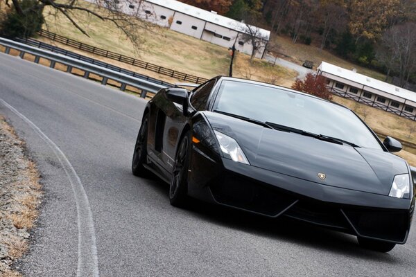 Un Lamborghini negro recorre la carretera con baches alrededor de los bordes en medio de un paisaje rústico otoñal