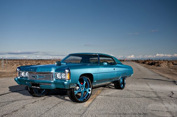 A blue car with blue discs is standing on an empty road