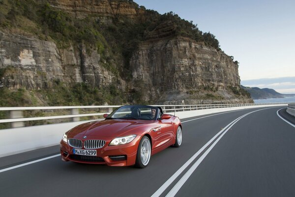 A red convertible is driving along a road in the middle of a picturesque area