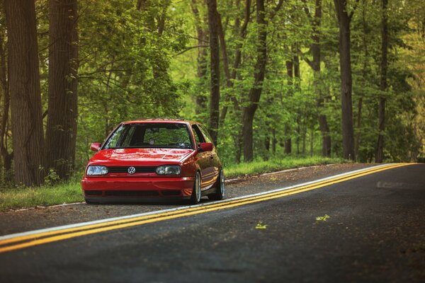 Un Volkswagen rojo monta en el camino en el bosque