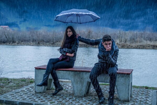 A girl and a guy are sitting on a bench in the rain