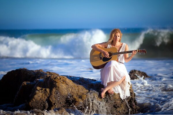 Mädchen mit Gitarre auf einem Stein am Meer