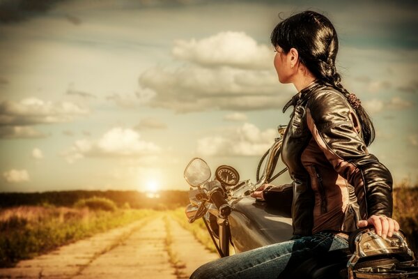 A girl on a motorcycle rides towards the sunset