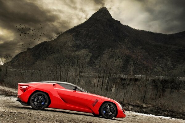 Concept-car rouge se dresse sur le gravier sur fond de montagne sombre