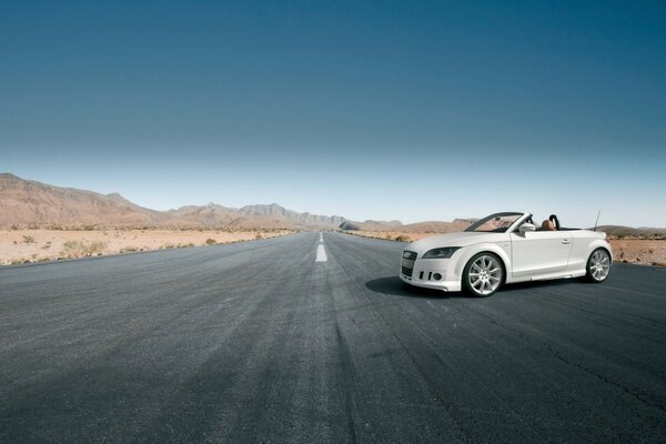 A chic white Audi convertible on a deserted gray road, against the background of mountains