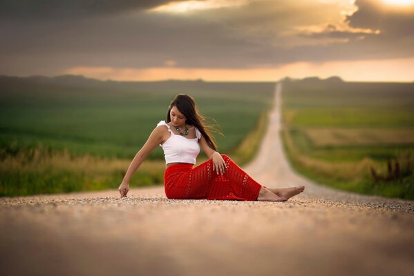 A girl is sitting in the middle of the road against the background of the evening sky