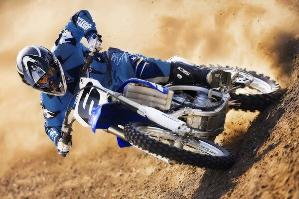 A motorcyclist in a blue suit and helmet rushes through the sand