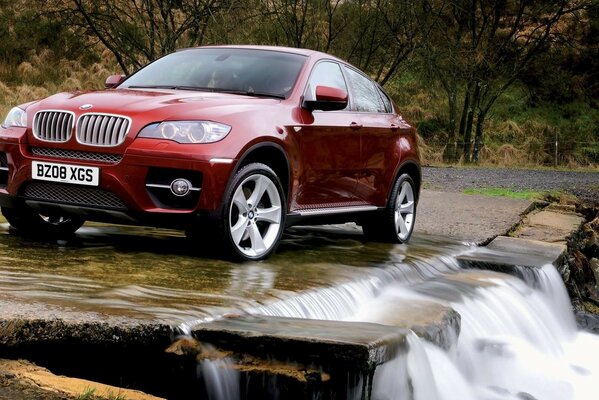 Red bmw in nature in front of a waterfall