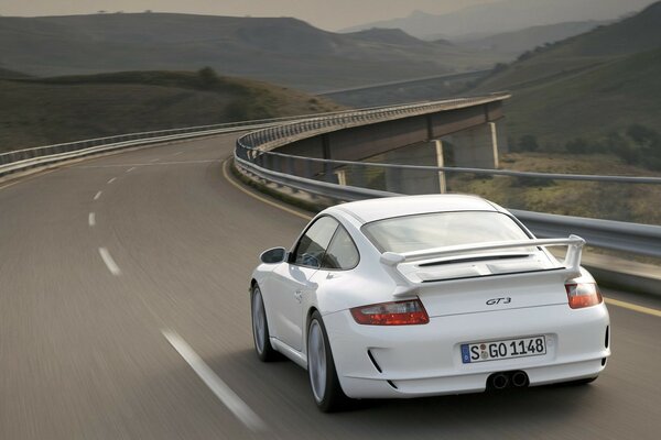 Porsche blanco 911 Gee 3 en la pista en el tráfico en el fondo del paisaje de montaña