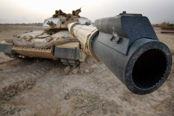 El cañón del cañón del tanque se dirige al marco contra el fondo de paisajes arenosos