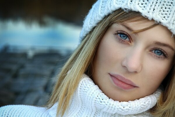 A girl with blue eyes in a white sweater and hat