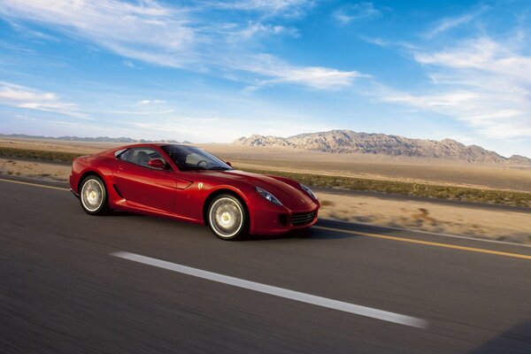 Ferrari rouge se précipite sur la route sur le fond de la montagne et le ciel bleu