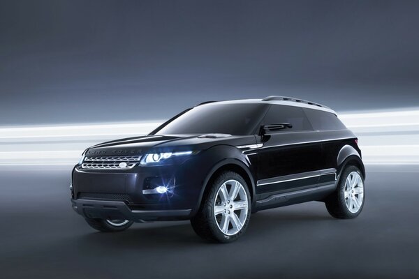 The Land Rover is black in a hangar with bright spotlights around the perimeter