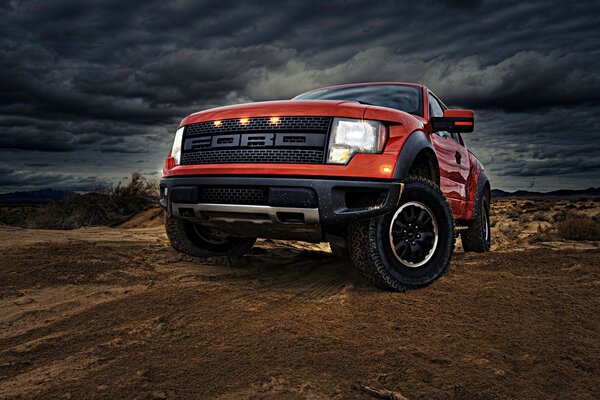 Red Ford car on the background of sand and clouds