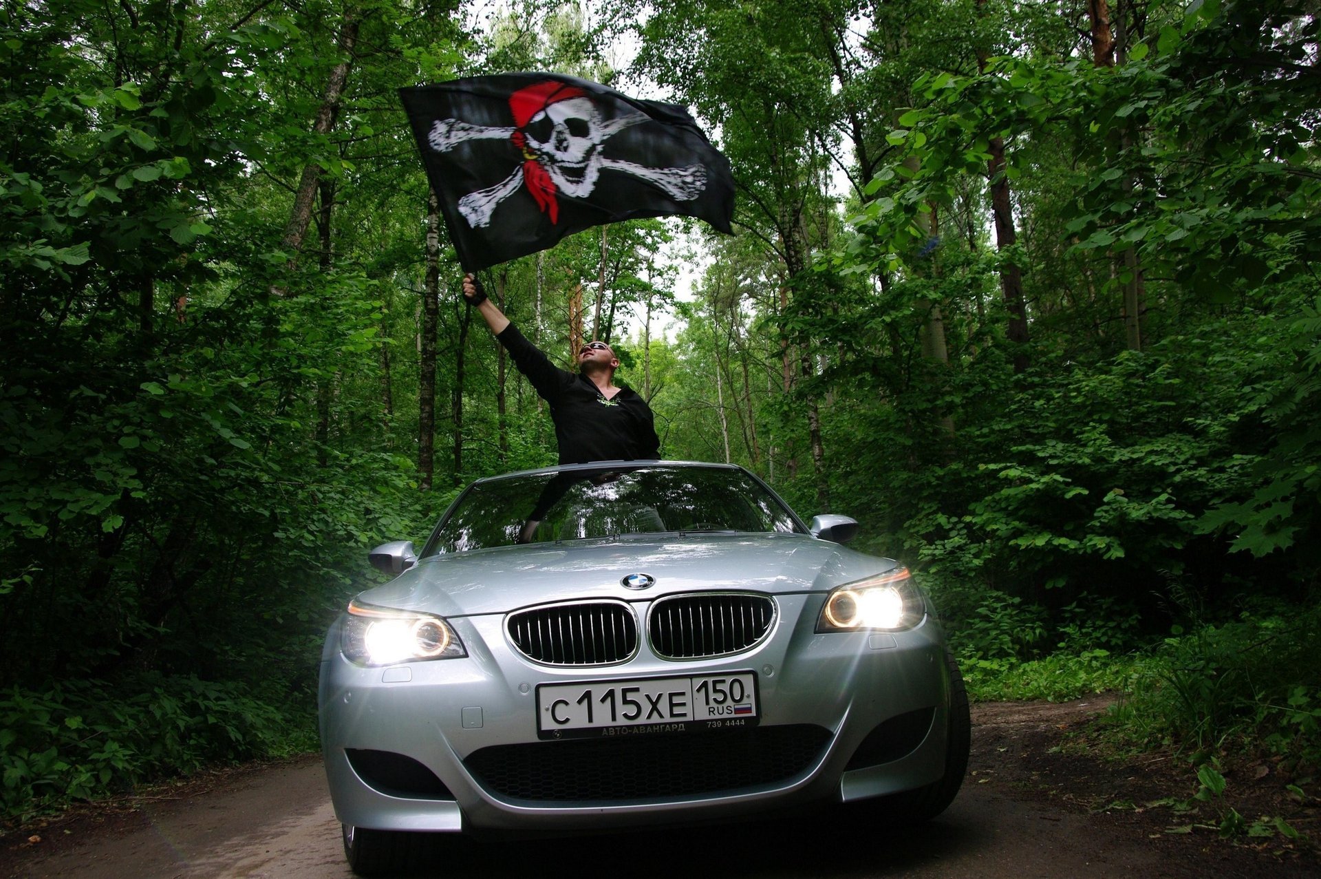 coloration grise homme avec drapeau drapeau noir crâne auto bmw verdure forêt nature phares voiture argentée voiture gars drapeau voitures transport véhicules