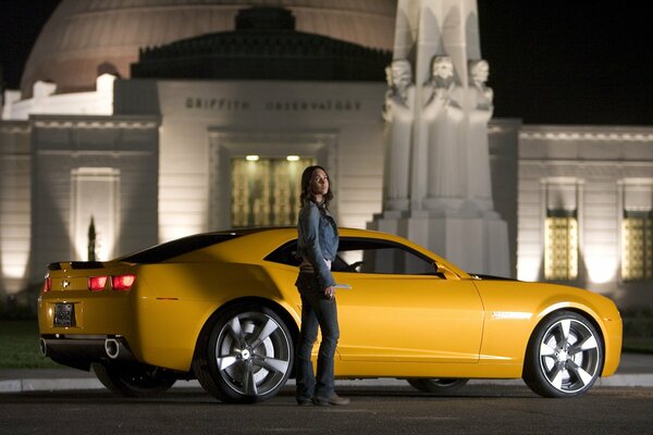 The girl is standing near the yellow car