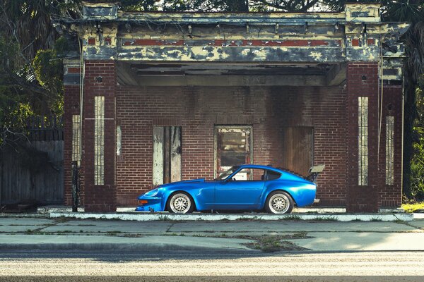 Chic blue datsun 240z on the background of an abandoned house