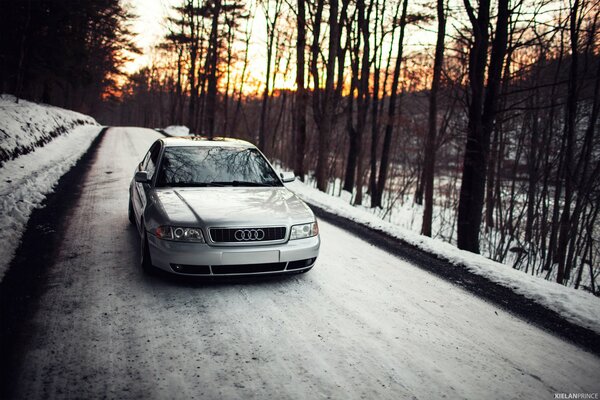 Sunset. white audi a4 on a snowy forest road