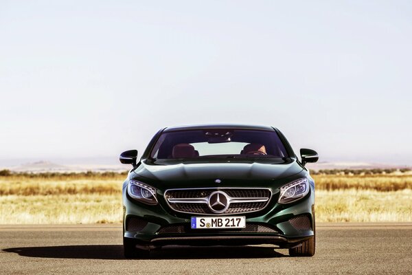 Black Mercedes rides on camera against the background of a field with yellow grass