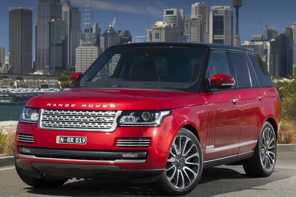 The red Range Rover is standing sideways and the city is behind it