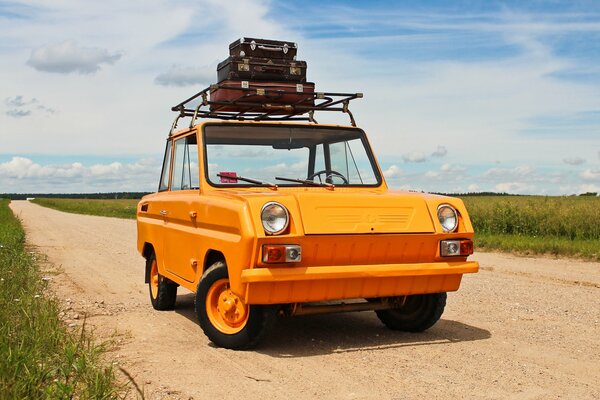 An unusual old orange car with suitcases on the roof