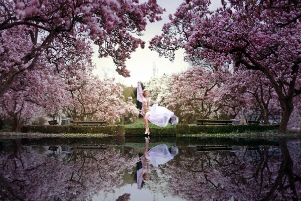 Fille dans le parc au bord du lac parmi les arbres en fleurs