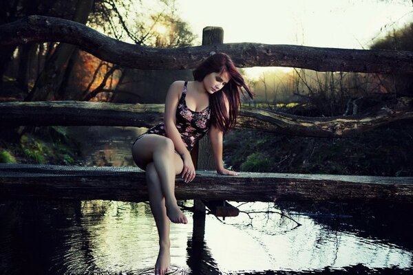 The brunette is sitting on the bridge at sunset