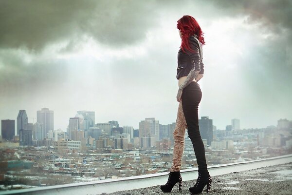 A model girl with red hair looks at a gray city