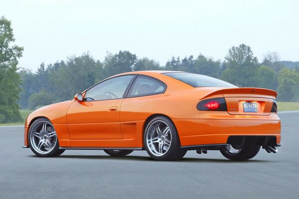 Pontiac naranja con discos grises contra el bosque