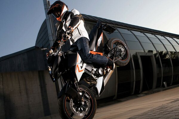 A motorcyclist stands on the front wheel of a KTM motorcycle